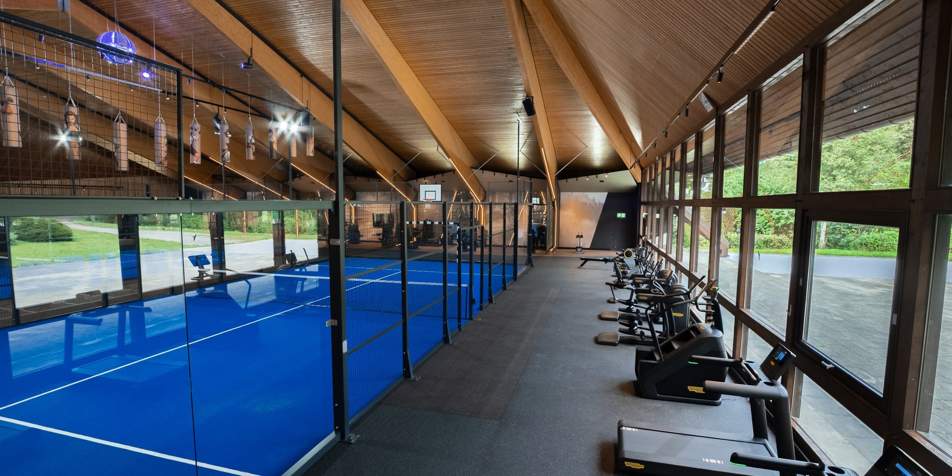 Kombination aus Padel-Platz und Fitnessbereich mit Laufbändern in der Sporthalle.