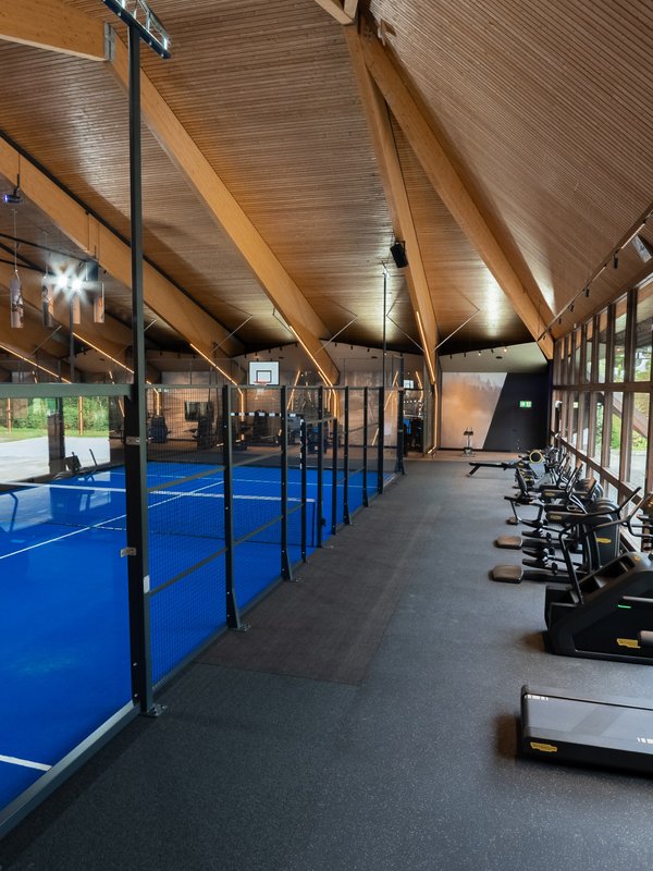 Kombination aus Padel-Platz und Fitnessbereich mit Laufbändern in der Sporthalle.