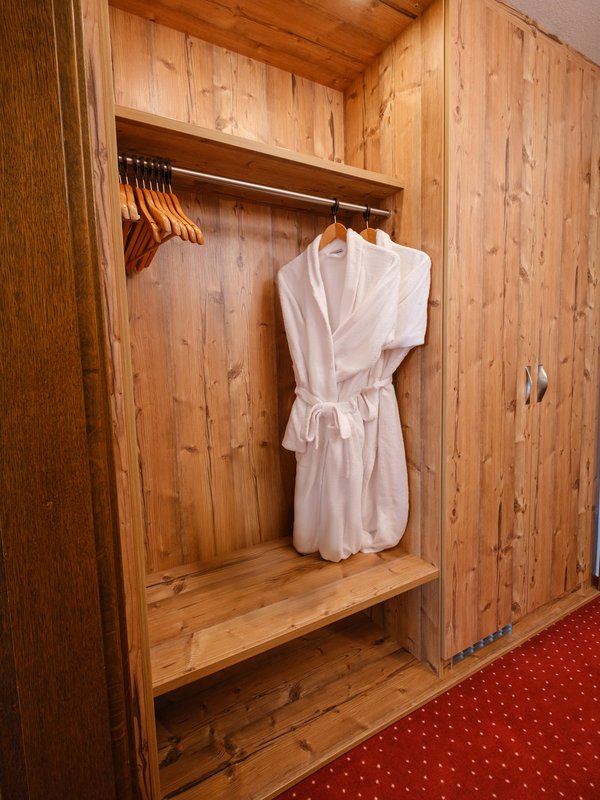 Ein flauschiger weißer Bademantel liegt bereit im hölzernen Schrank des Wellnessbereichs im Hotel Vier Jahreszeiten am Schluchsee.