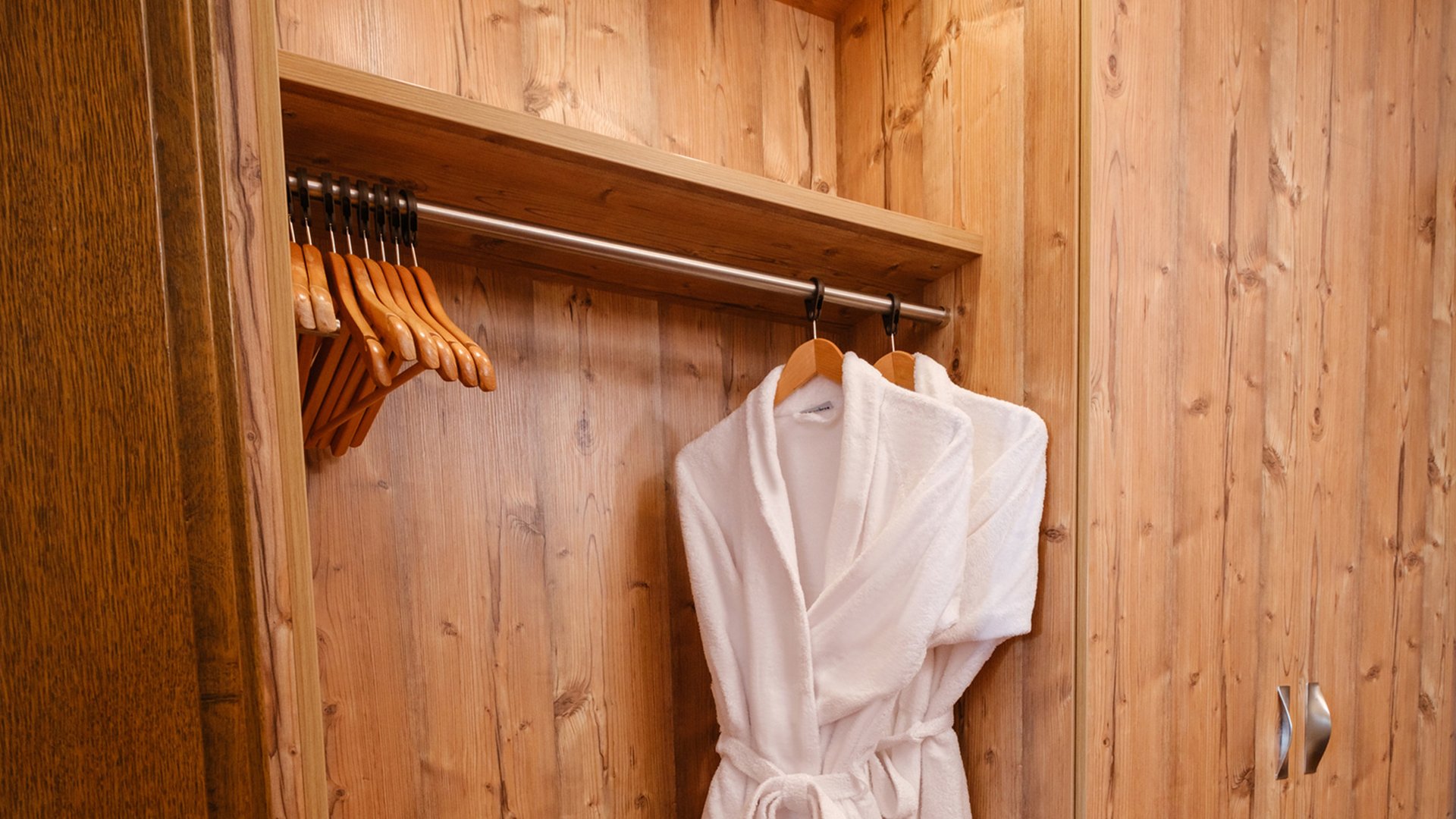 Ein flauschiger weißer Bademantel liegt bereit im hölzernen Schrank des Wellnessbereichs im Hotel Vier Jahreszeiten am Schluchsee.