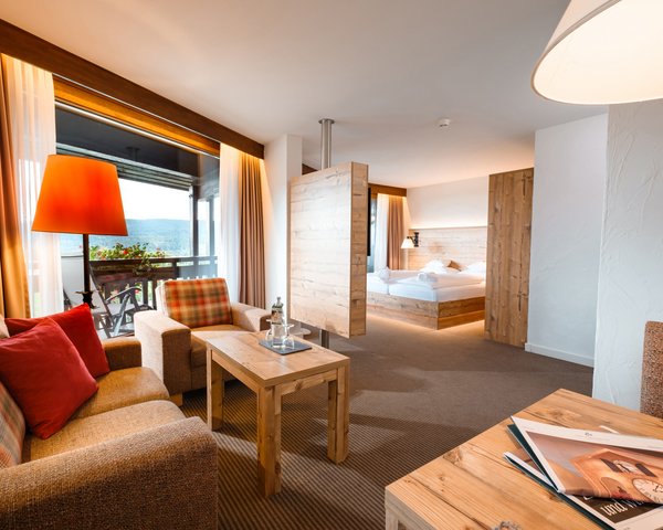 Wohnzimmer mit warmem Lichtkonzept und Blick in den Schlafbereich im Hotel Vier Jahreszeiten am Schluchsee.