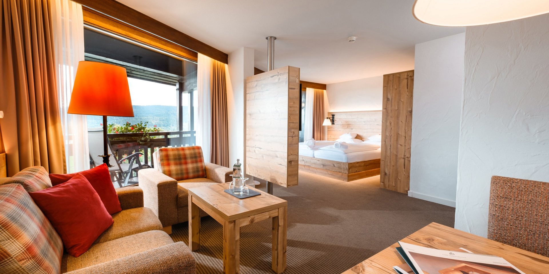 Wohnzimmer mit warmem Lichtkonzept und Blick in den Schlafbereich im Hotel Vier Jahreszeiten am Schluchsee.