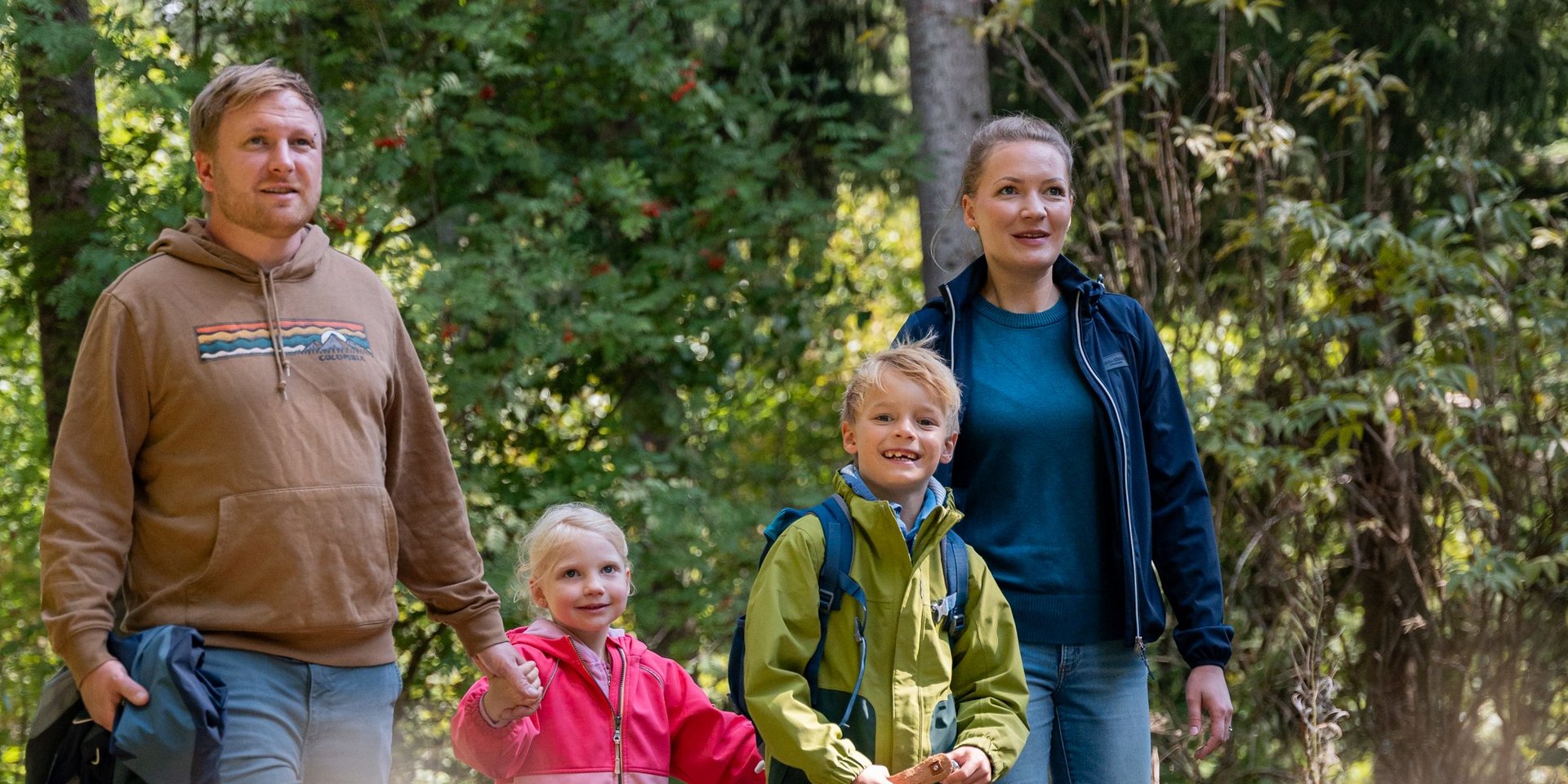 Eine Familie wandert gemeinsam auf einem sonnigen Pfad durch das Hotelgelände am Schluchsee.