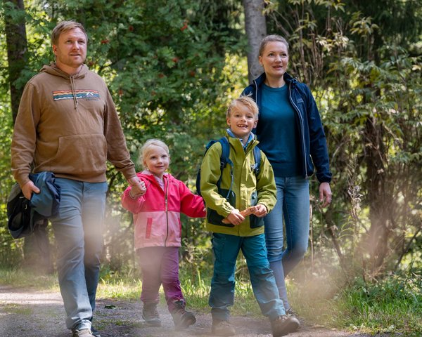 Eine Familie wandert gemeinsam auf einem sonnigen Pfad durch das Hotelgelände am Schluchsee.