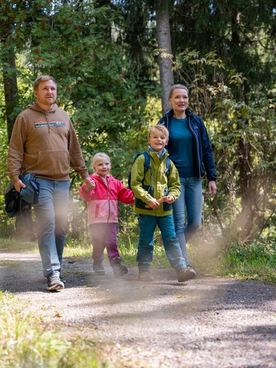 Eine Familie wandert gemeinsam auf einem sonnigen Pfad durch das Hotelgelände am Schluchsee.