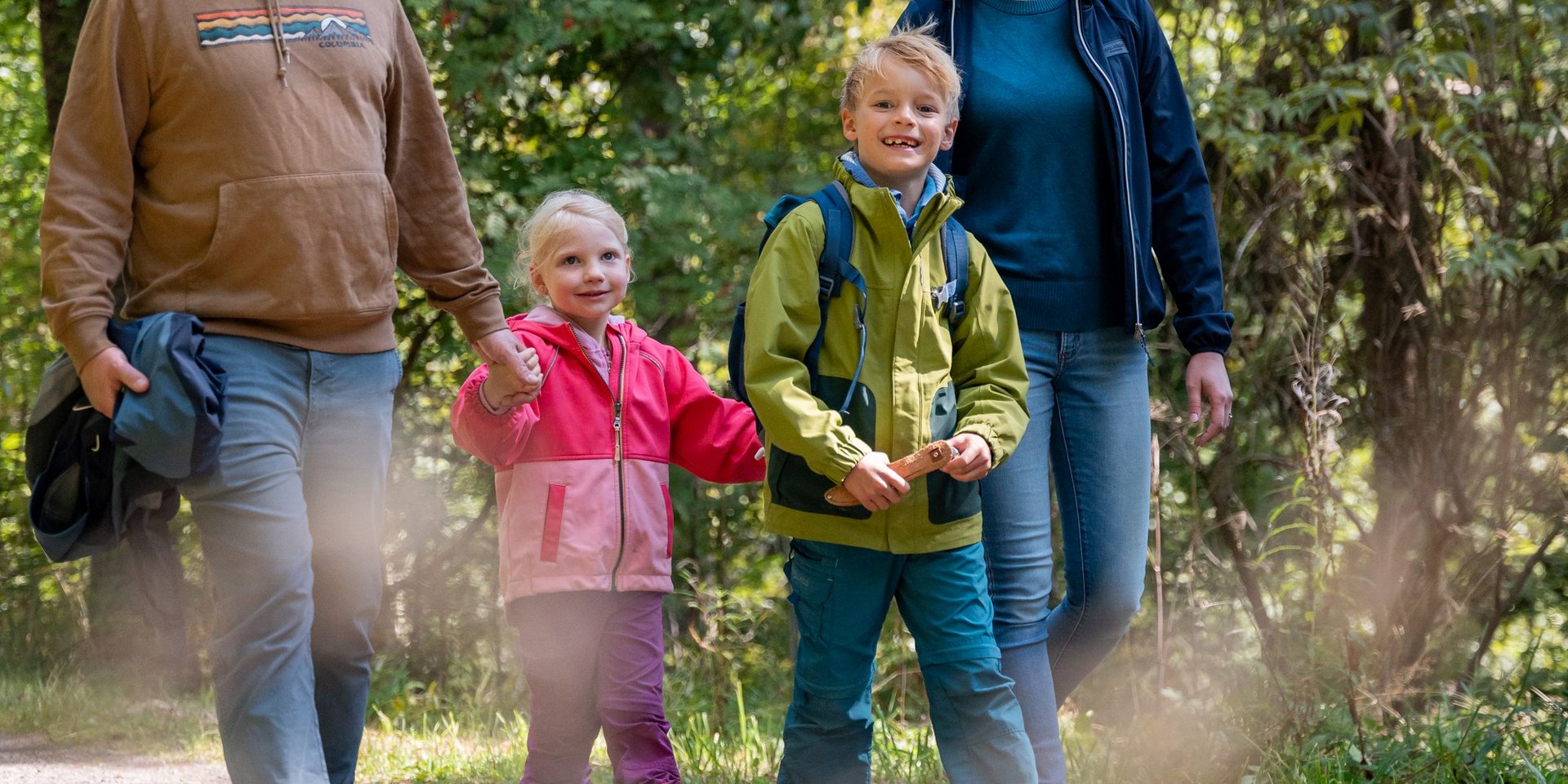 Eine Familie wandert gemeinsam auf einem sonnigen Pfad durch das Hotelgelände am Schluchsee.