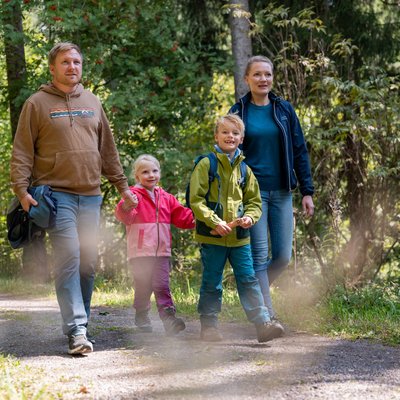 Eine Familie wandert gemeinsam auf einem sonnigen Pfad durch das Hotelgelände am Schluchsee.