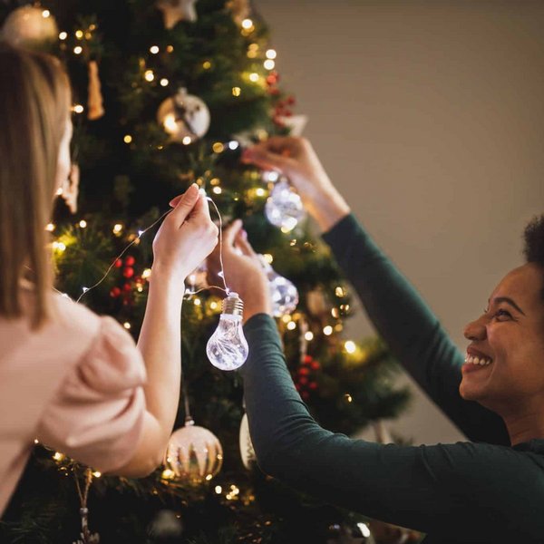 Zwei Frauen schmücken gemeinsam lachend einen Weihnachtsbaum mit silbernen Kugeln.