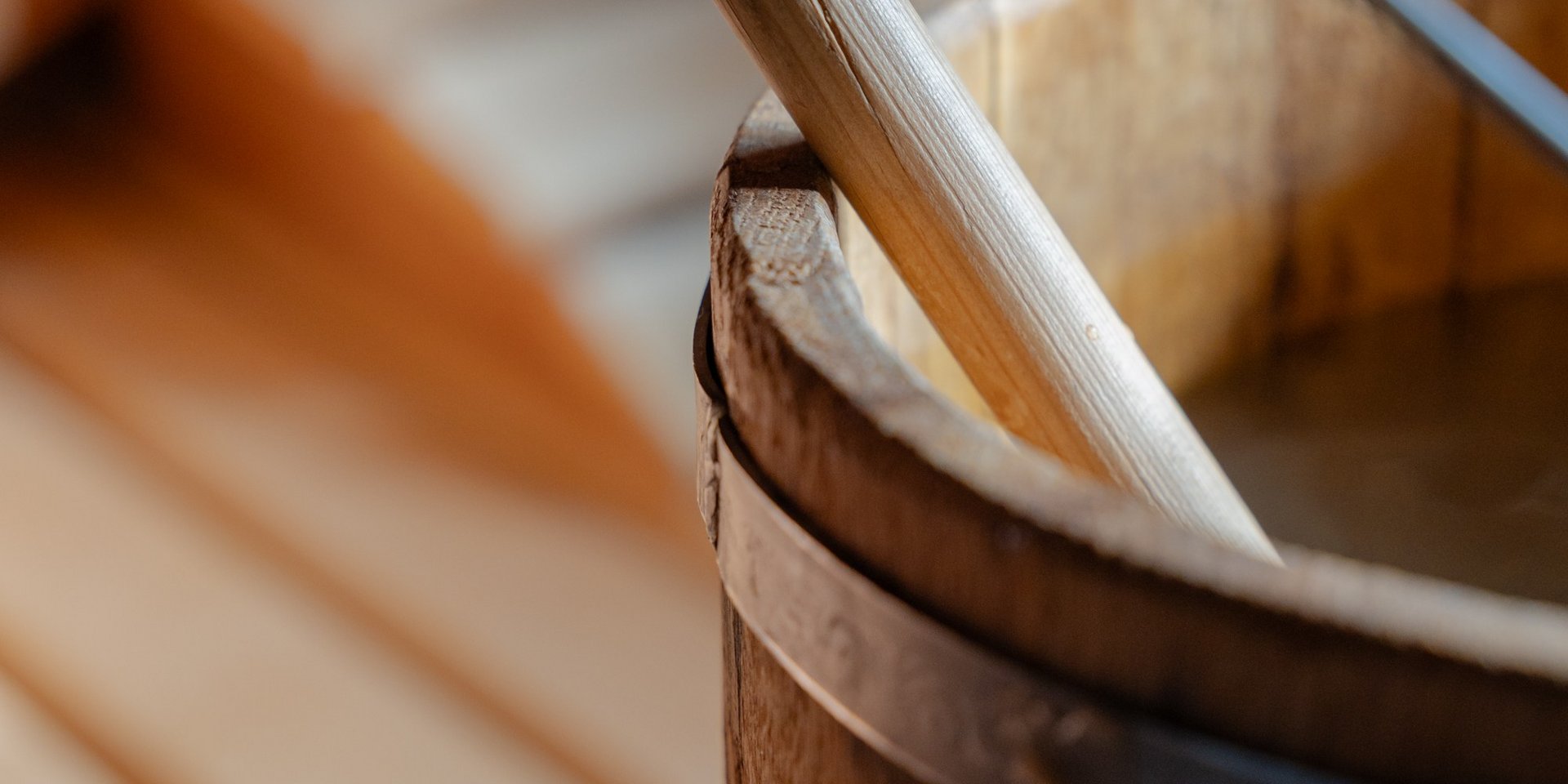 Klassisches Saunazubehör: Ein hölzerner Aufgusseimer mit Kelle vor den Saunabänken.