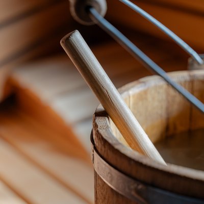 Klassisches Saunazubehör: Ein hölzerner Aufgusseimer mit Kelle vor den Saunabänken.