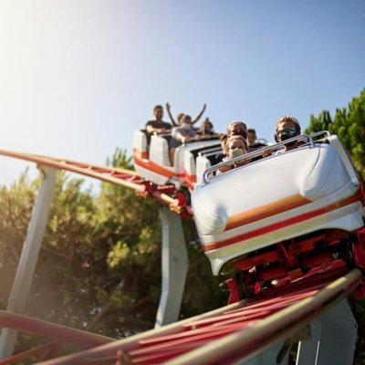 Eine Achterbahn fährt mit hoher Geschwindigkeit durch einen Looping in einem sonnigen Freizeitpark.