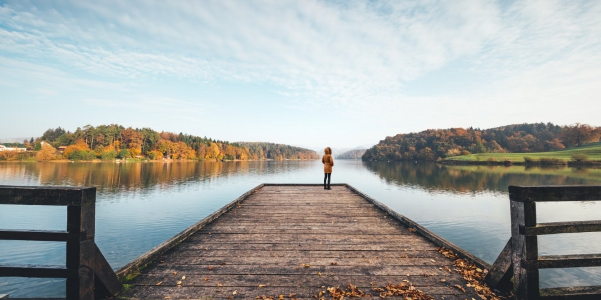 Ein langer Holzsteg führt weit hinaus auf einen ruhigen See im herbstlichen Schwarzwald.