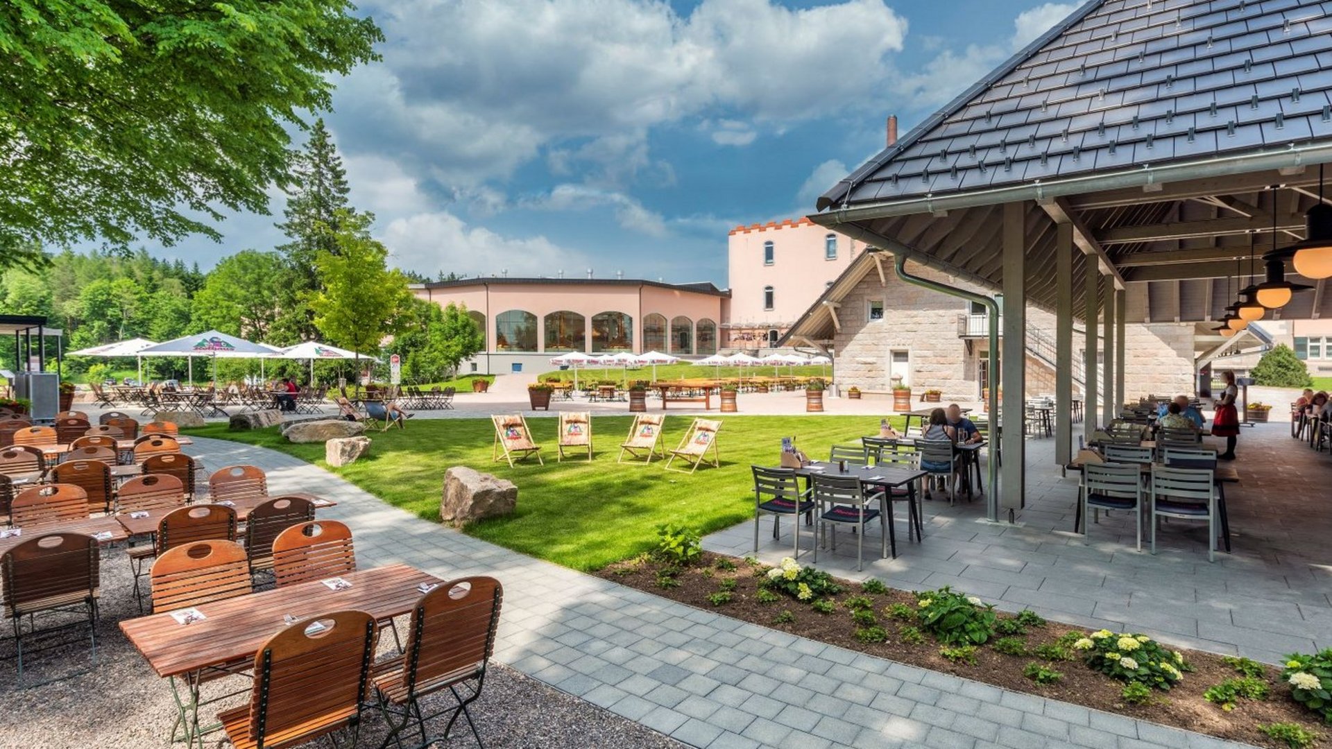 Ein Biergarten mit verschiedenen Stühlen und der Brauerei im Hintergrund