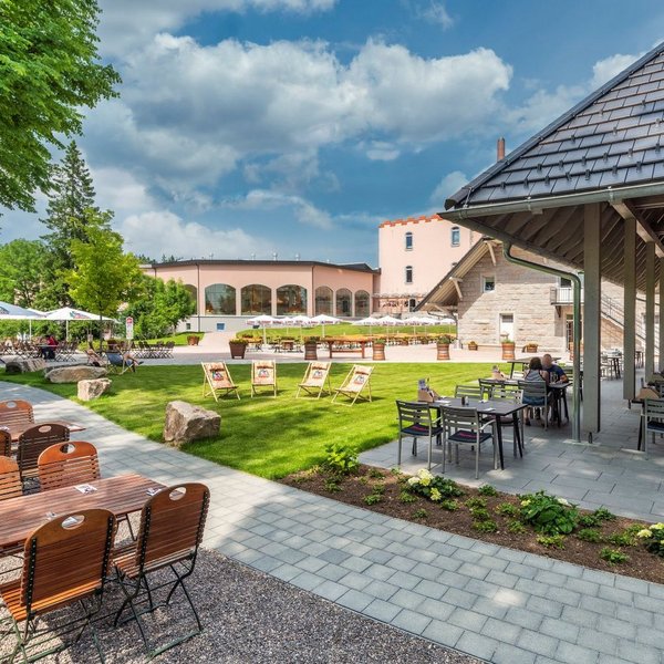 Ein Biergarten mit verschiedenen Stühlen und der Brauerei im Hintergrund