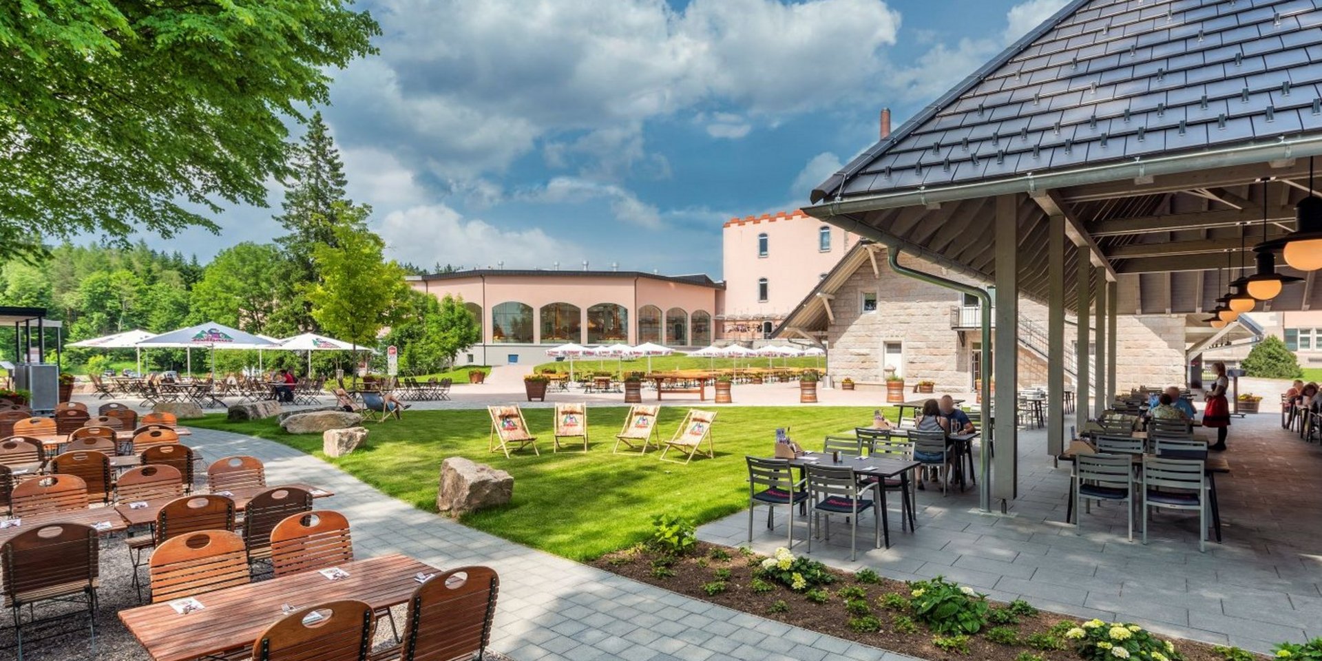 Ein Biergarten mit verschiedenen Stühlen und der Brauerei im Hintergrund
