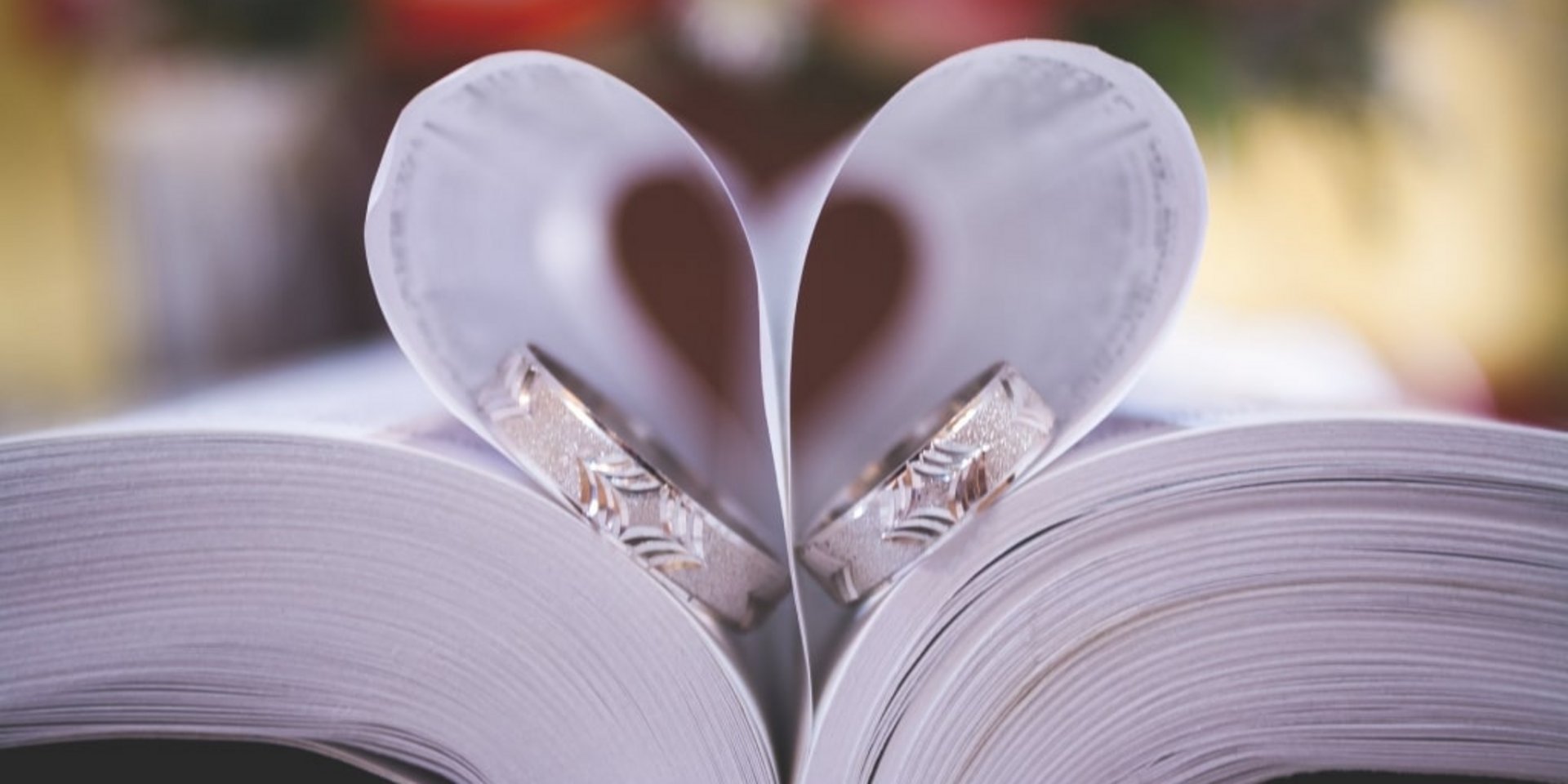 Zwei Eheringe liegen in der Mitte eines Buches, dessen Seiten zu einer Herzform gebogen sind.