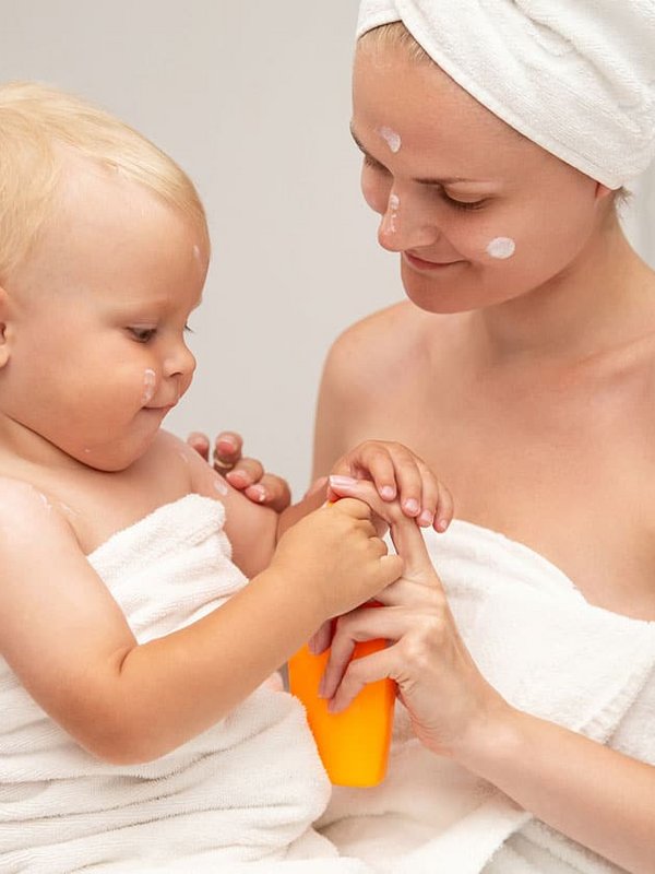 Eine Mutter hält ihr Kleinkind nach dem Baden liebevoll in ein weißes Handtuch eingewickelt.