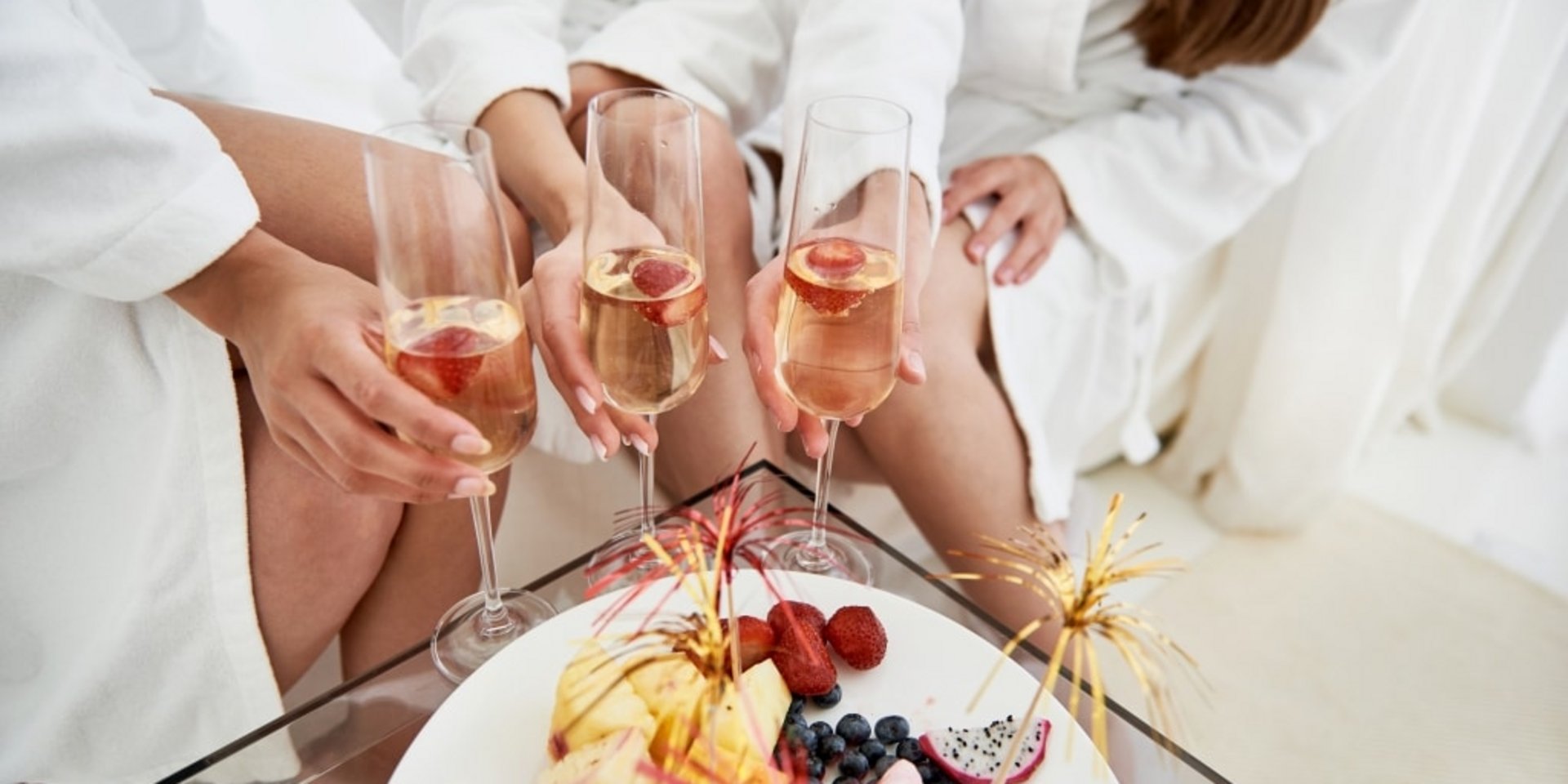 Eine Gruppe von Frauen in weißen Bademänteln stößt mit Sektgläsern auf einen gemeinsamen Wellnesstag an.