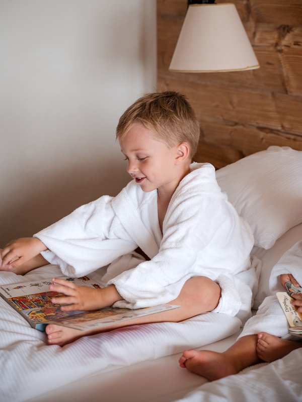 Ein kleiner Junge genießt die Zeit im weichen Bett einer Familiensuite im Hotel Vier Jahreszeiten am Schluchsee.