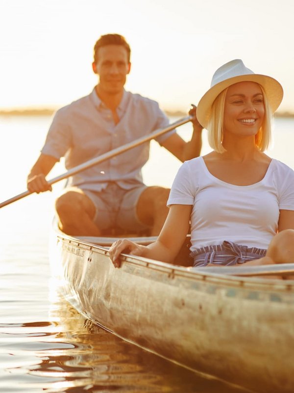 Ein Paar genießt eine ruhige Bootsfahrt in einem Holzkanu auf einem See bei Sonnenuntergang.