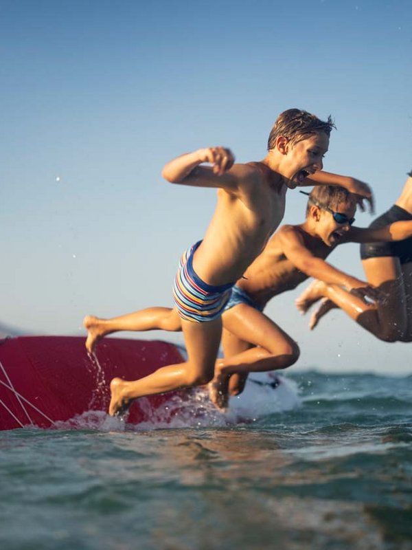 Drei Kinder springen gleichzeitig mit viel Freude von einem SUP.