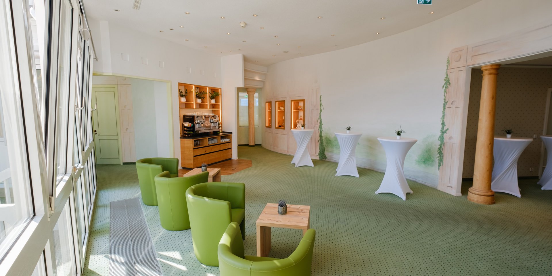 Großzügiges, lichtdurchflutetes Foyer mit grünen Sesseln und Stehtischen für Networking-Pausen im Hotel Vier Jahreszeiten im Schwarzwald.
