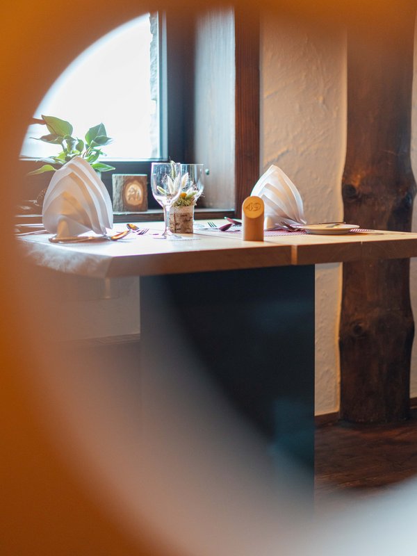 Blick durch eine herzförmige Öffnung eines Stuhles auf einen gedeckten Holztisch im rustikalen Schwiizer Stübli im Hotel Vier Jahreszeiten am Schluchsee.