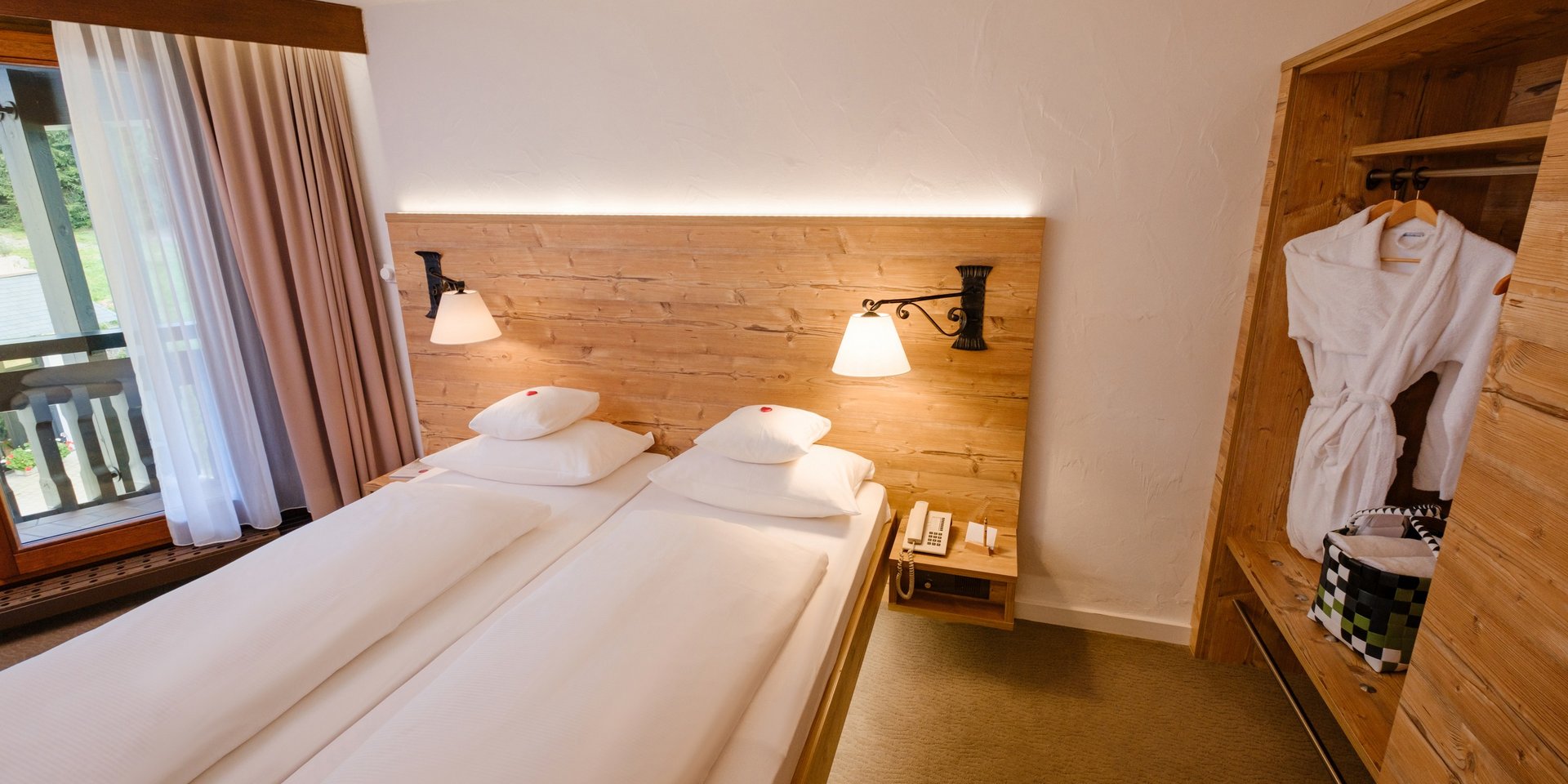 Komfortables Doppelbett im Schwarzwald-Stil mit Blick auf den Kleiderschrank und bereitgelegte Bademäntel.