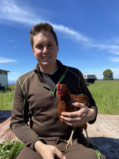 Porträt von Robin Vogelbacher mit einem Huhn auf dem Schoß.
