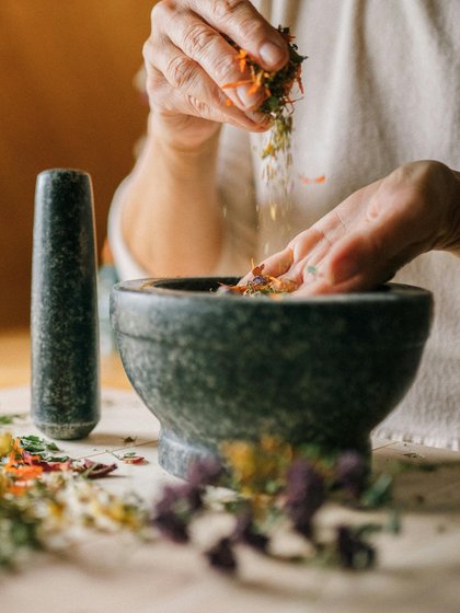 Ein Mörser und über ihm zwei Hände die Gewürze streuen