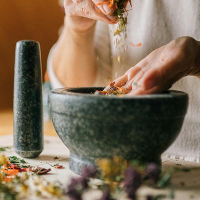 Ein Mörser und über ihm zwei Hände die Gewürze streuen
