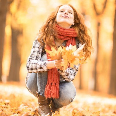 Frau im Herbstlaub mit Blättern in der Hand