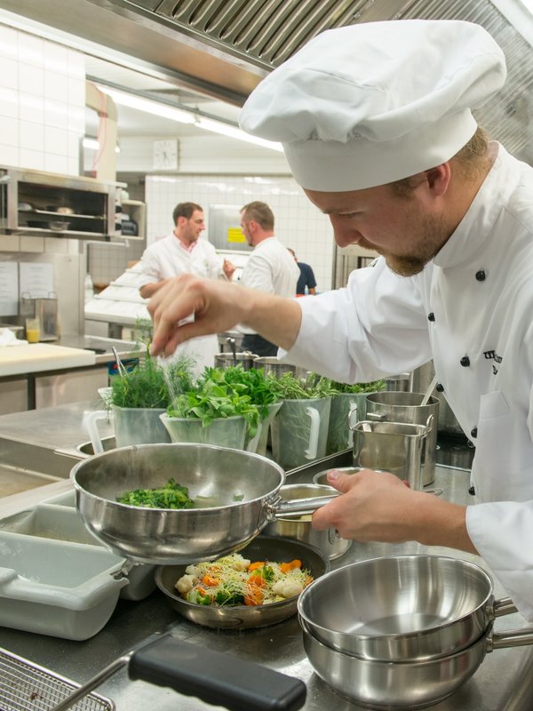 Ein professioneller Koch in weißer Uniform richtet konzentriert Speisen in der Küche des Hotels Vier Jahreszeiten an.