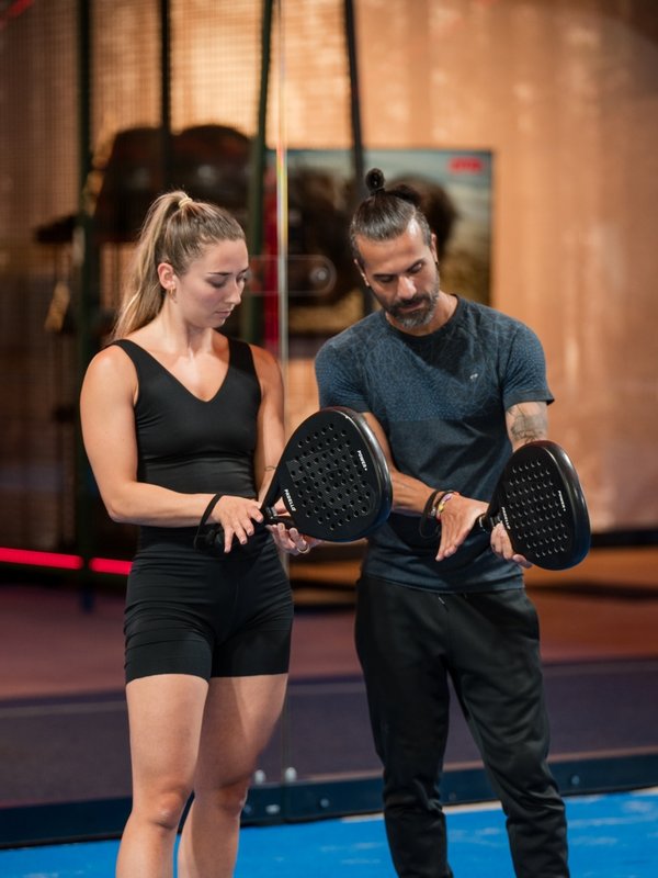 Ein Trainer erklärt zwei Gästen die richtige Schlägerhaltung für Padel-Tennis.