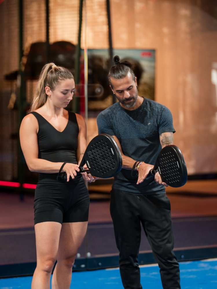 Ein Trainer erklärt zwei Gästen die richtige Schlägerhaltung für Padel-Tennis.