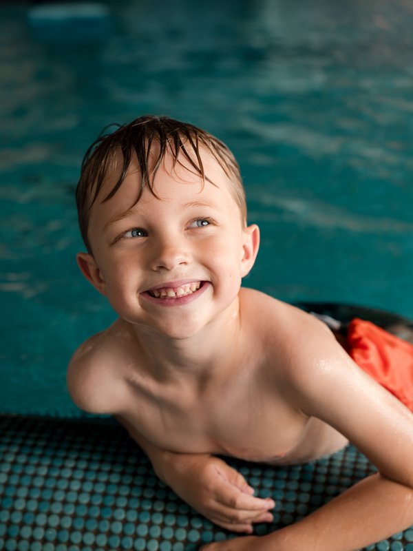 Junge grinst aus dem Beckenrand beim Schwimmtraining