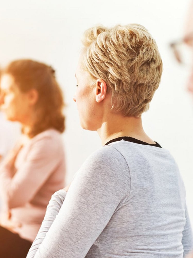Eine Gruppe von Frauen praktiziert gemeinsam Yoga in einem hellen, sonnigen Kursraum.