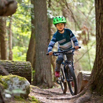 Ein Junge mit Helm und Sportkleidung bei einer Mountainbike-Tour durch den dichten Tannenwald.