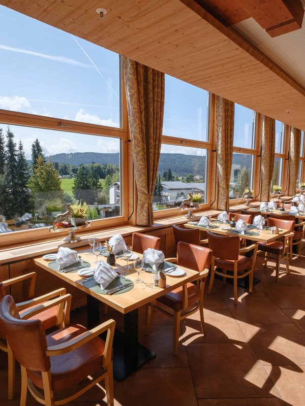 Lichtdurchfluteter Restaurantbereich mit eingedeckten Tischen und Blick auf den Schwarzwald im Hotel Vier Jahreszeiten am Schluchsee.