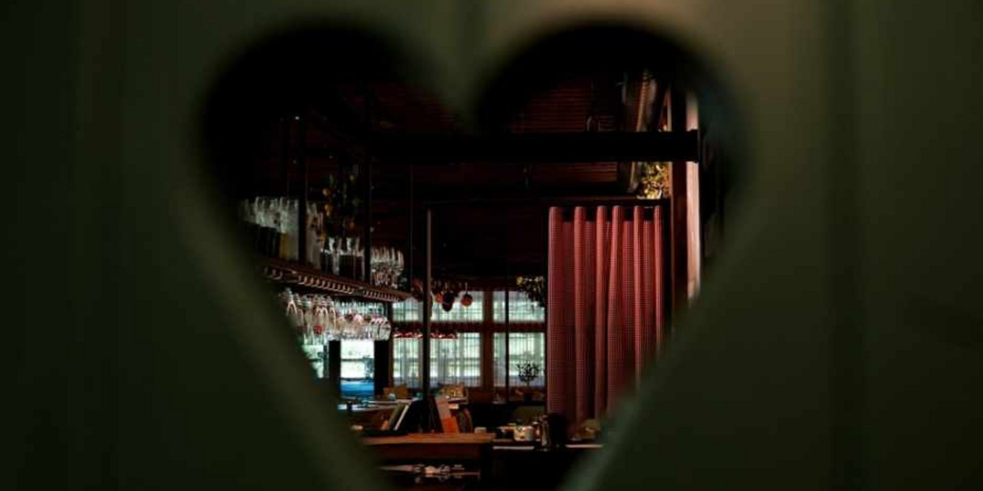Romantisches Detail: Herzförmiger Ausschnitt in einer grünen Holztür mit Blick in das Restaurant.