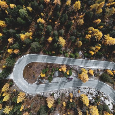 Luftaufnahme einer Haarnadelkurve einer Straße, die mitten durch einen herbstlichen Wald führt.