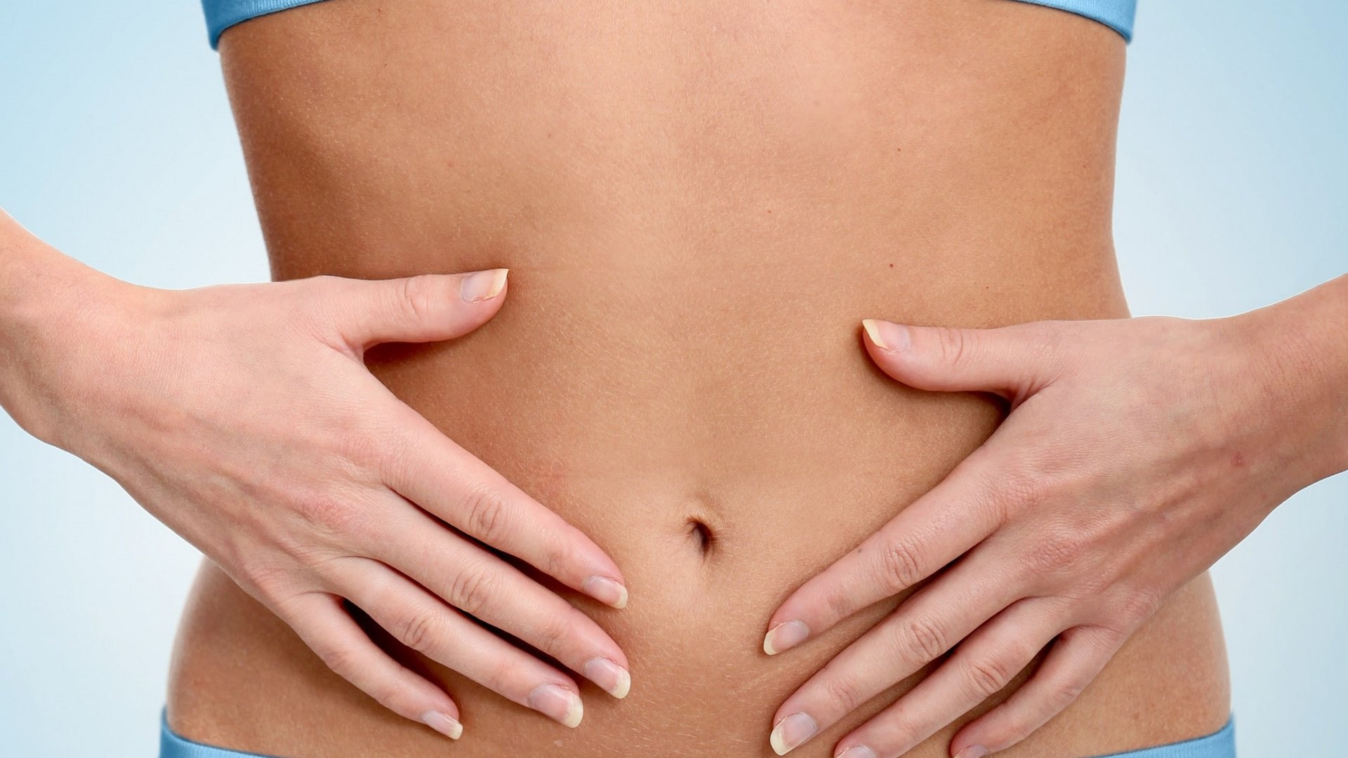 Detailaufnahme einer Frau, die ihre Hände sanft auf ihren flachen Bauch legt (Wellness-Kontext).