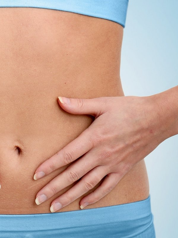 Detailaufnahme einer Frau, die ihre Hände sanft auf ihren flachen Bauch legt (Wellness-Kontext).