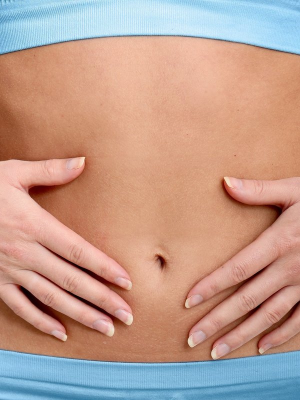 Detailaufnahme einer Frau, die ihre Hände sanft auf ihren flachen Bauch legt (Wellness-Kontext).