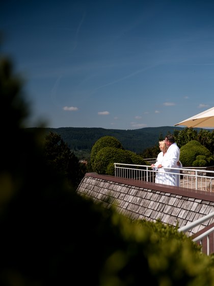Paar auf Hotelterasse, blauer Himmel und ein Gebüsch