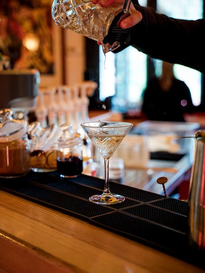 Ein Barkeeper bei der präzisen Zubereitung eines Drinks vor der gläsernen Kulisse der Hotelbar.