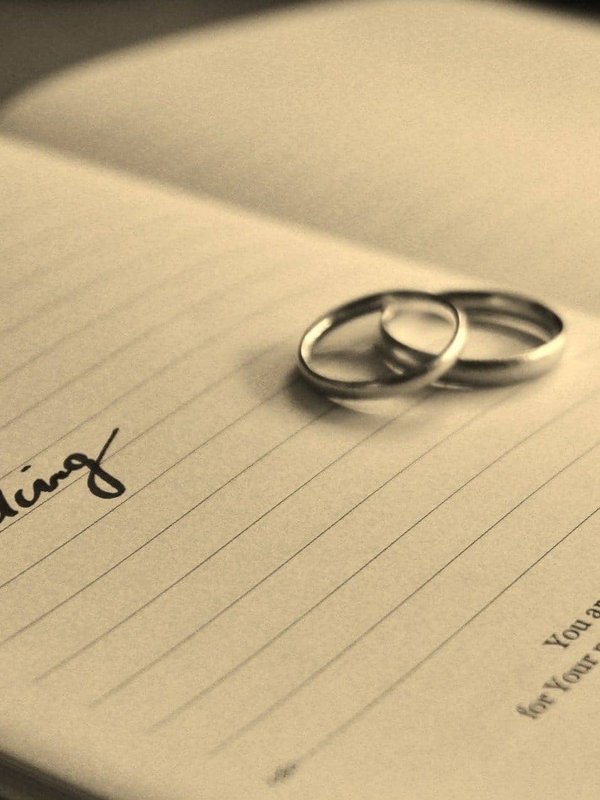 Zwei silberne Eheringe liegen auf einem aufgeschlagenen Buch mit dem Wort Wedding.