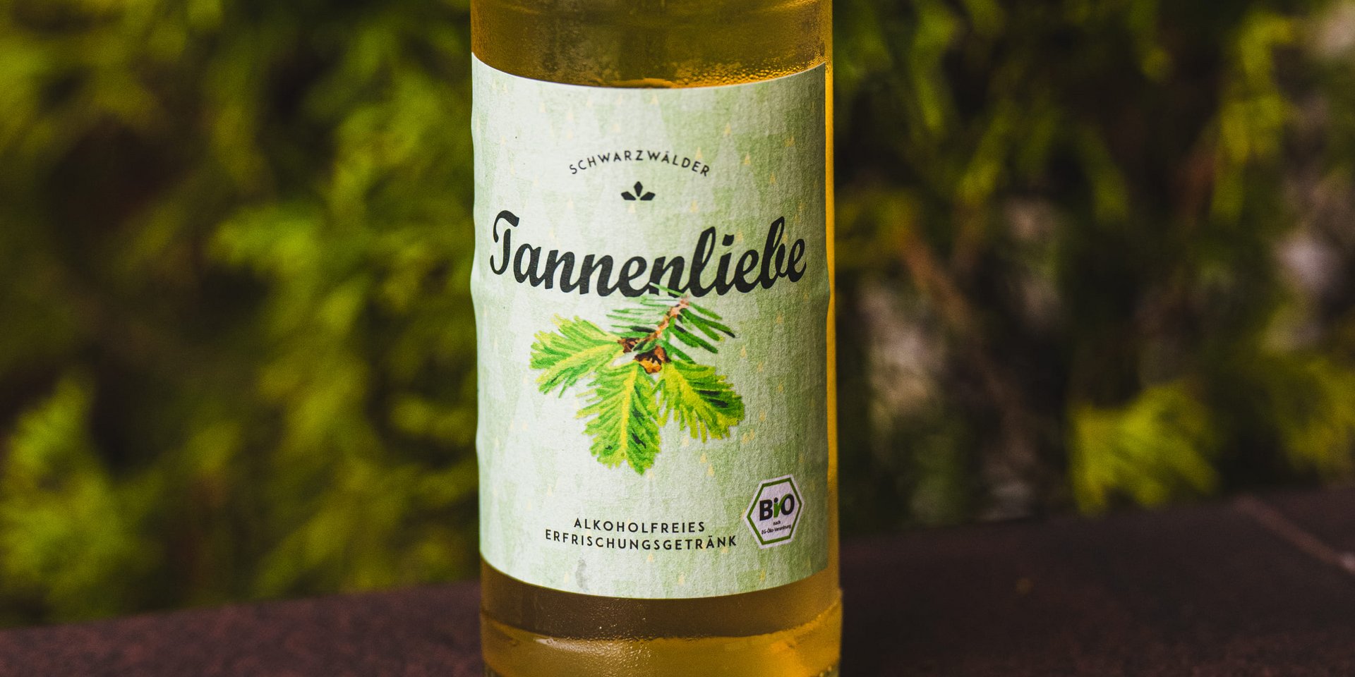 Eine Flasche „Tannenliebe“ Limonade vor der Kulisse eines Schwarzwälder Nadelwaldes.