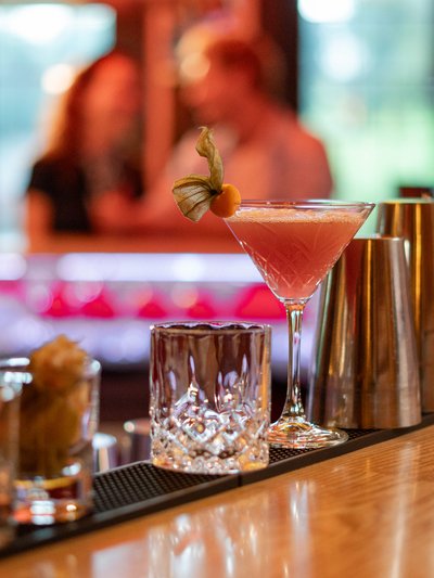Ein eleganter pinkfarbener Cocktail serviert auf dem Holztresen der hoteleigenen Bar.