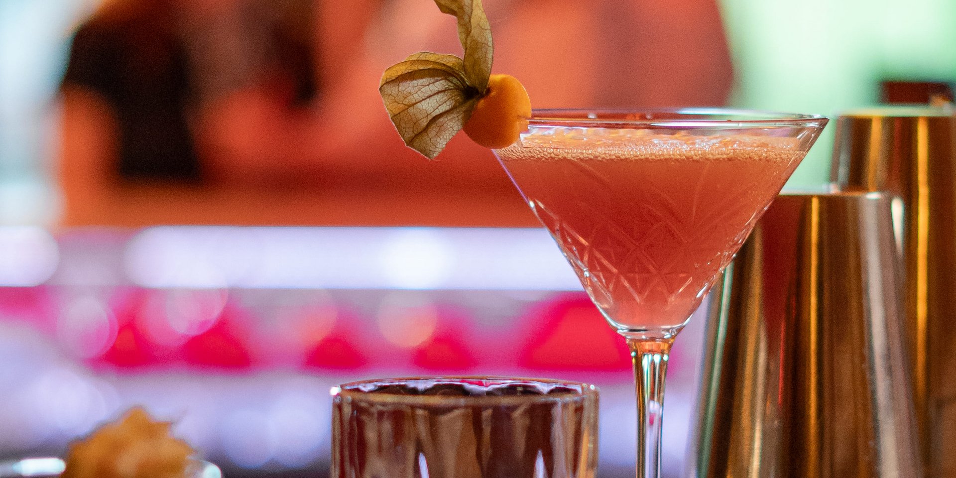 Ein eleganter pinkfarbener Cocktail serviert auf dem Holztresen der hoteleigenen Bar.